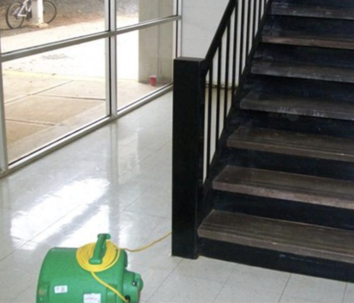 Green SERVPRO air mover on floor by a staircase.
